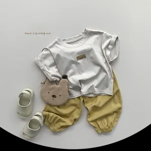 Flat lay of kids summer set with white t-shirt, yellow pants and bear crossbody bag