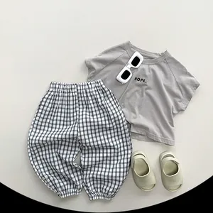 Mise à plat d'un t-shirt enfant taupe imprimé HOPE et d'un pantalon de jogging à carreaux