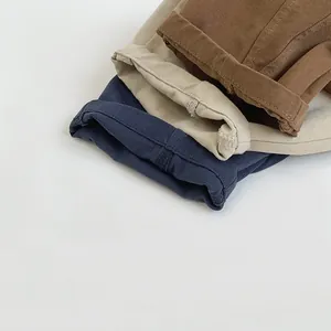 Détail de pantalons en coton empilés en bleu marine, beige et marron avec ourlets roulés