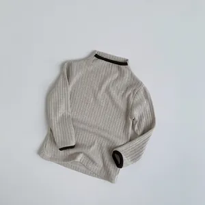 Detail of knit child sweater with contrast brown piping on high neck and cuffs