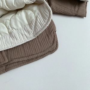 Detail of children's quilted jacket featuring brown pleated fabric and cream lining