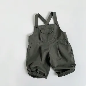 Detail of olive green cotton overalls featuring front pocket and buttoned rolled cuffs