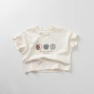 Detail of baby cotton T-shirt featuring artistic apple prints and slogan on cream fabric