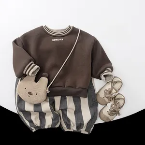 Flat lay of kid's dark brown sweatshirt with Sunday print and gray striped fleece pants