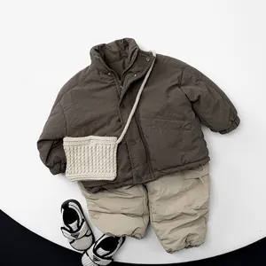 Flat lay of brown puffer jacket, beige pants, knit bag, and sneakers on round white stage