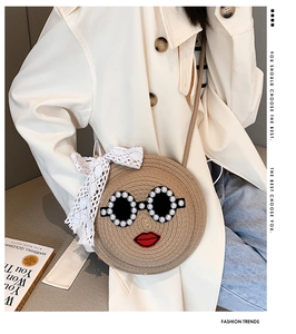 Detail of round woven straw bag featuring cartoon face with pearl sunglasses and lace bow