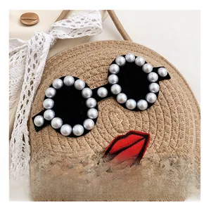 Detail showing the woven texture, pearl-edged glasses design, and red embroidery on straw bag
