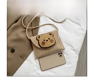 Detail of hand-woven straw crossbody bag with cute bear patch next to a smartphone