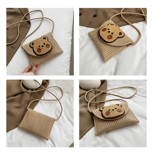 Detail of woven straw envelope bag featuring a 3D plush bear patch and textured cotton rope