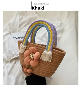 Dettaglio della borsa in paglia kaki con manico arcobaleno intrecciato, nappa bianca e fiore rosa