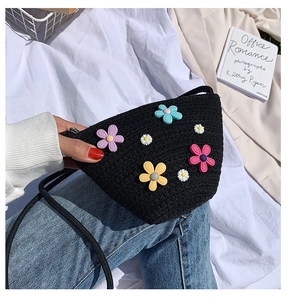 Détail d'un sac en paille noire tissé main avec fleurs 3D colorées dans un cadre décontracté