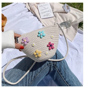Détail du sac à bandoulière en paille avec broderies florales sur fond d'herbe