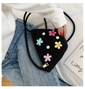Détail d'un sac noir en paille tressée avec fleurs 3D colorées et bandoulière corde
