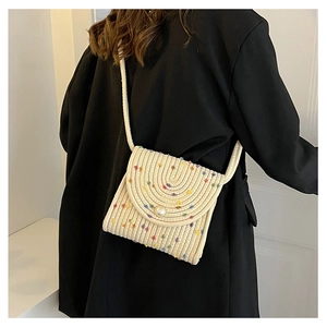 Dettaglio borsa a tracolla in cotone intrecciato con pompon colorati e chiusura con perla