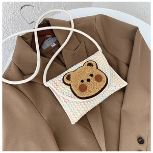 Detail of white woven envelope bag with cute teddy bear patch and zigzag pattern