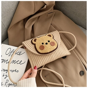 Detail of beige woven straw envelope bag featuring a cute teddy bear patch on trench coat