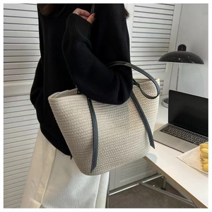 Close-up of beige woven tote bag with contrasting black leather straps and white stitching