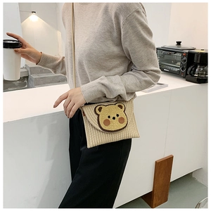 Detailed close-up of woven beige envelope bag with cute plush bear on soft strap