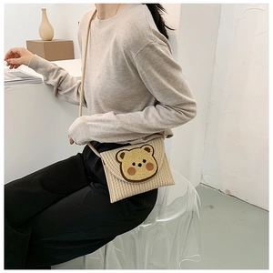 Detail view of woven straw envelope bag featuring a cute 3D cartoon bear patch