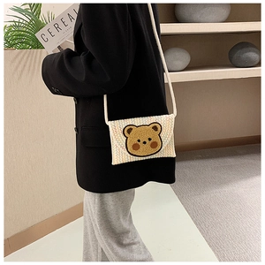 Detailed view of beige woven envelope crossbody bag with a cute plush bear decoration