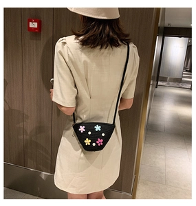 Détail d'un sac bandoulière en paille noire avec fleurs 3D colorées sur un mannequin