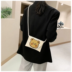Detailed back view of a woven straw envelope bag with a cute bear embroidery on a model