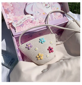 Détail du sac à bandoulière en paille tressée avec fleurs colorées dans un coffret cadeau rose