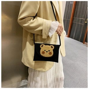 Detail shot of a black knit envelope bag featuring a 3D teddy bear patch on the front