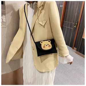 Close-up of black woven crossbody envelope bag with cute 3D teddy bear patch decoration