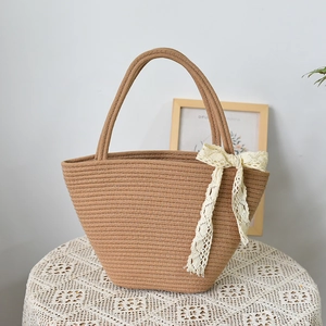 Handwoven straw tote bag with cream lace bow decoration on a rustic white lace tabletop