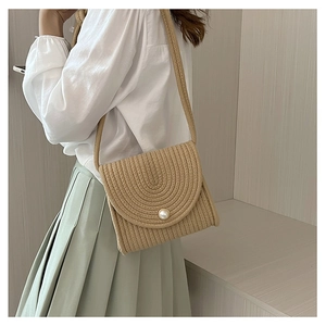 Dettaglio di borsa a busta intrecciata a mano in cotone con perla bianca su patta beige