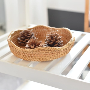 Handcrafted round woven rattan tray with wavy edges and decorative pinecones on a wood surface