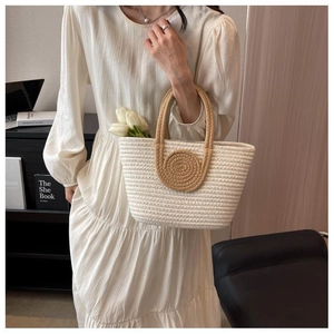 Detail of cream woven tote bag with brown circular handles held by model in dress