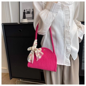 Detail of rose red woven shoulder bag decorated with a floral silk bow on a model