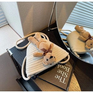 Détail d'un sac bandoulière tissé crème avec un joli petit ours en peluche marron en décoration