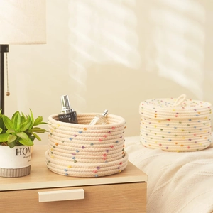 Detail view of woven cotton rope storage baskets with colorful pom poms on wooden surface