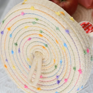 Close-up of woven storage basket lid with colorful pom poms and a sturdy top handle