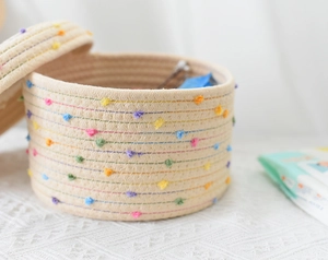 Detailed close-up of woven cotton rope storage basket with colorful pom poms and lid