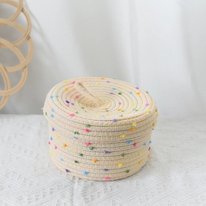 Detail view of woven storage basket featuring colorful pom-poms and a practical top handle