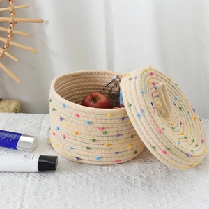 Close-up of woven storage basket with colorful pom-poms and lid on lace surface