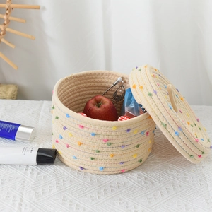 Detailed close-up of woven cotton storage basket with colorful pompoms and matching lid