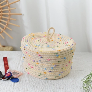 Close-up of woven cotton rope storage basket with colorful pom poms and handle lid
