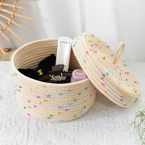 Detail of hand-woven cotton rope storage basket with colorful pom-poms and lid handle