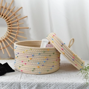 Detail of woven cotton rope storage basket with colorful pompoms and lid handles