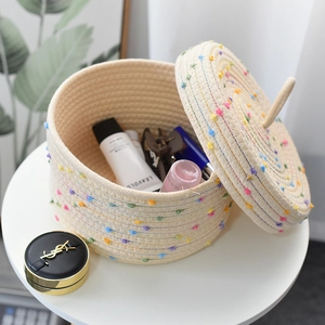 Detailed close-up of woven cotton rope storage basket with colorful pom poms and lid