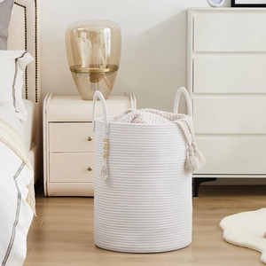Detailed view of a white cotton rope laundry basket with tassel and beige knit blanket