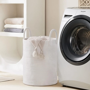 Close-up of white woven cotton rope laundry basket with reinforced handles and tassel decor