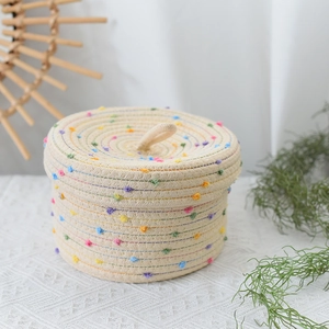 Detail of hand-woven cotton storage basket featuring colorful pom-poms and a lid