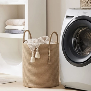 Large woven storage basket with tassels and handles for laundry organization in home bedroom