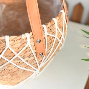 Close-up of woven straw plant basket featuring white cotton mesh and leather handle detail